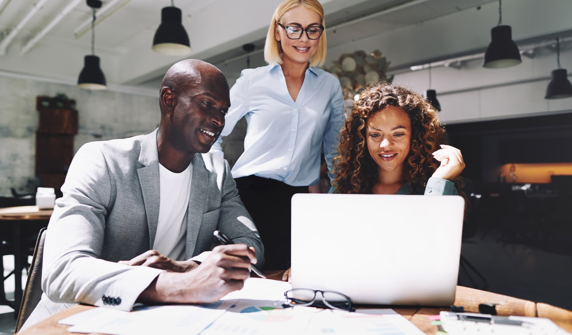 3 young professionals crowd around a laptop smiling